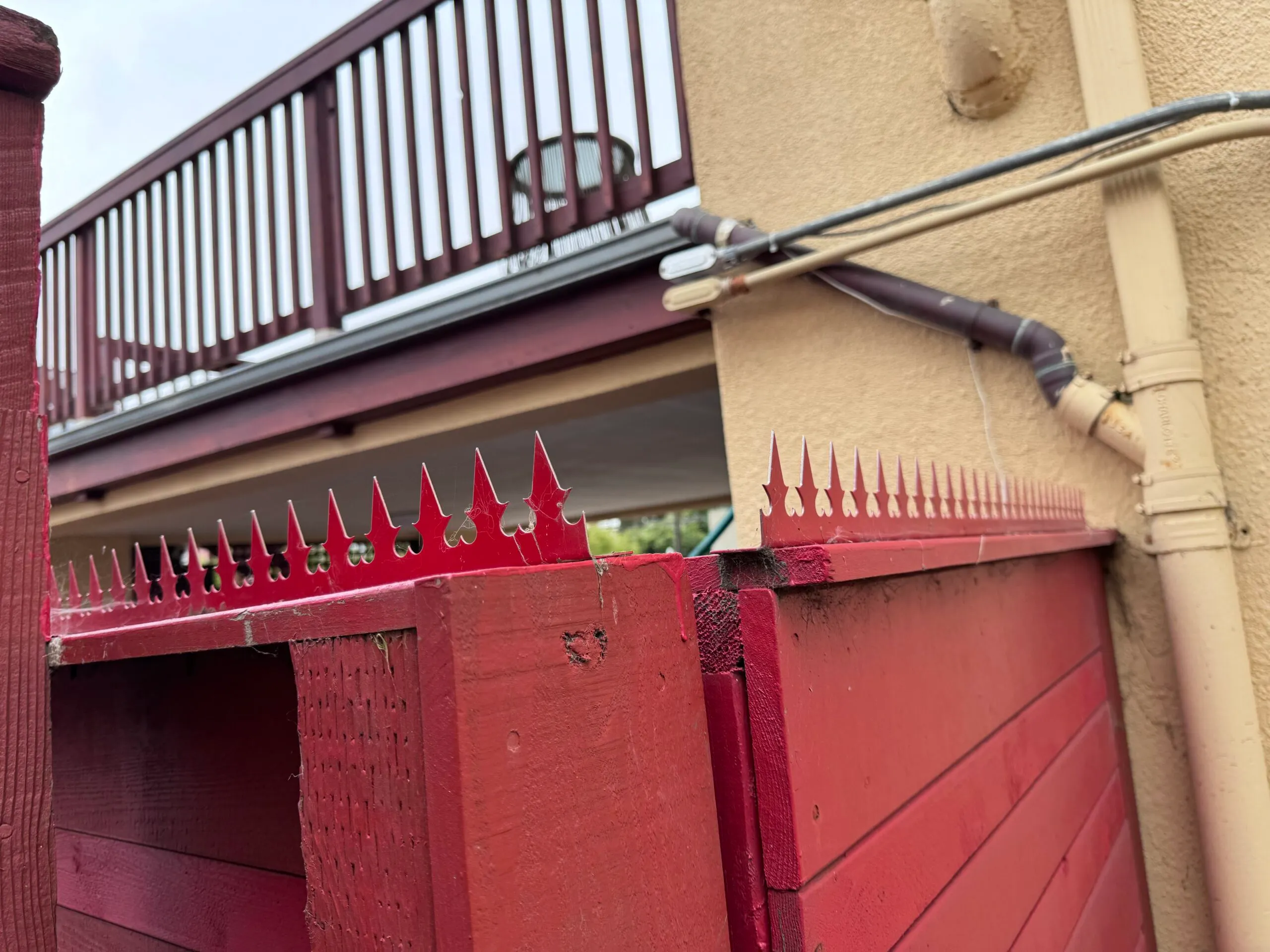Full view of the red wooden fence and red spikes, with a balcony railing visible in the background.