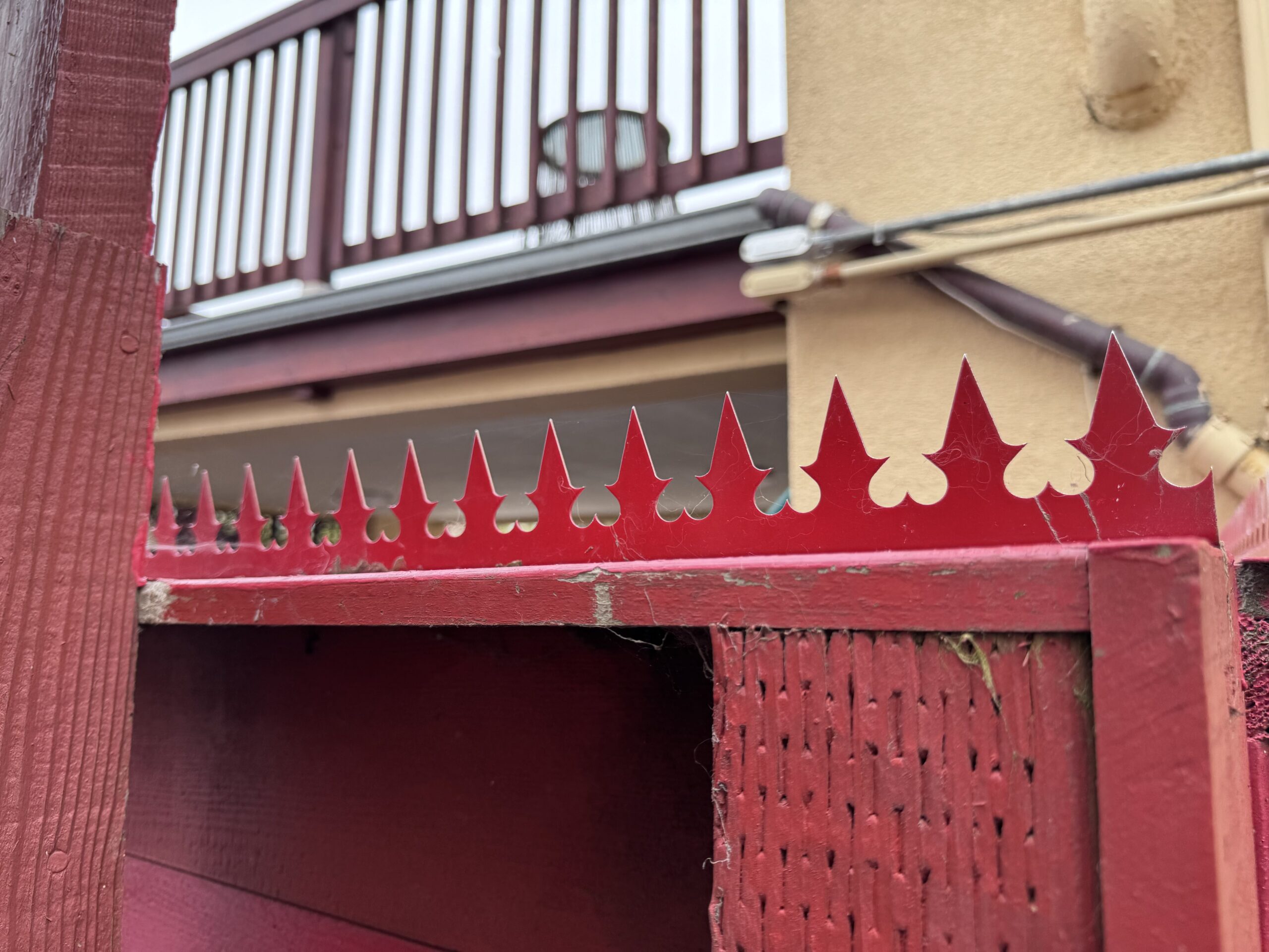 Eckdetail des Zauns. Das Verhältnis zwischen roten Spikes und angrenzender Außenwand ist erkennbar.