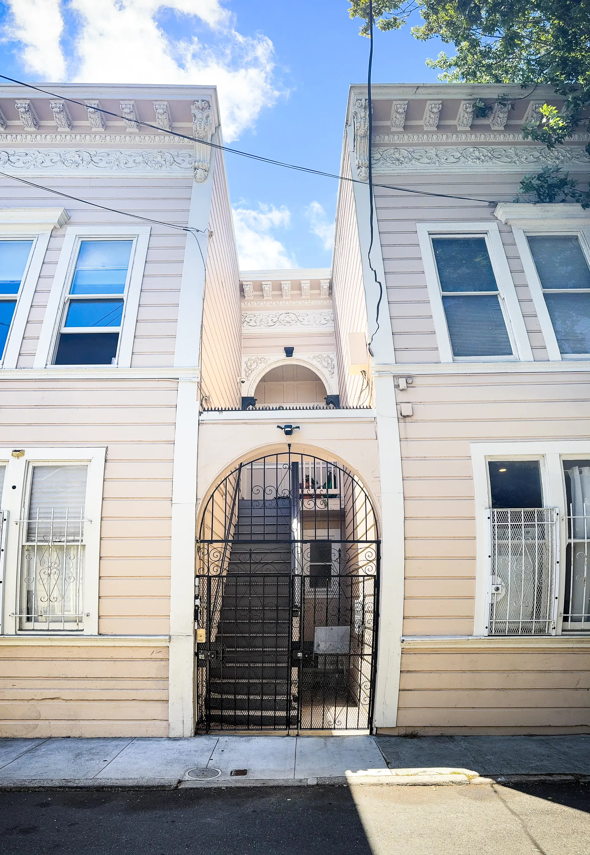 Classically detailed ivory apartment facade in San Francisco with bay windows and a recessed arched entry protected by a black wrought iron gate.