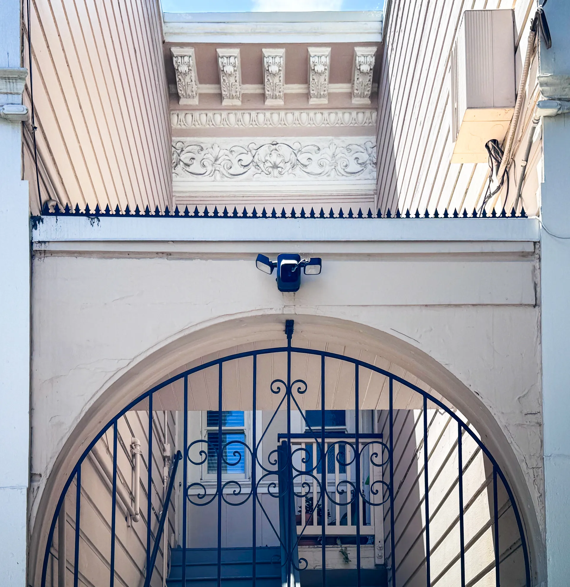 Frontal view of the arched entry: spiral-patterned wrought iron gate, Gothic Black Dual Blade spike line, and carved classical cornice above.