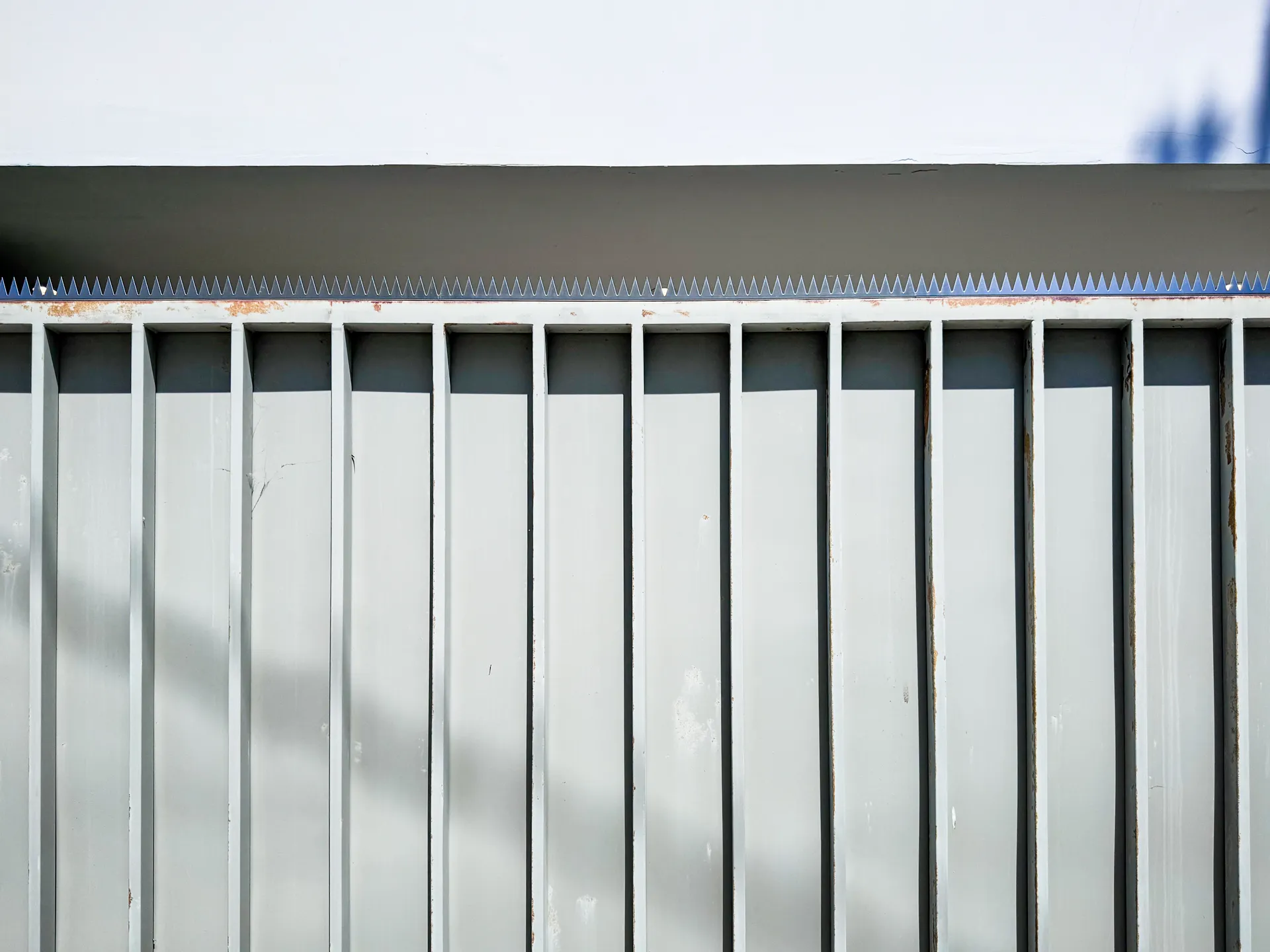 Close-up of the fence top, showing continuous spikes and the shadow cast by the white eaves.