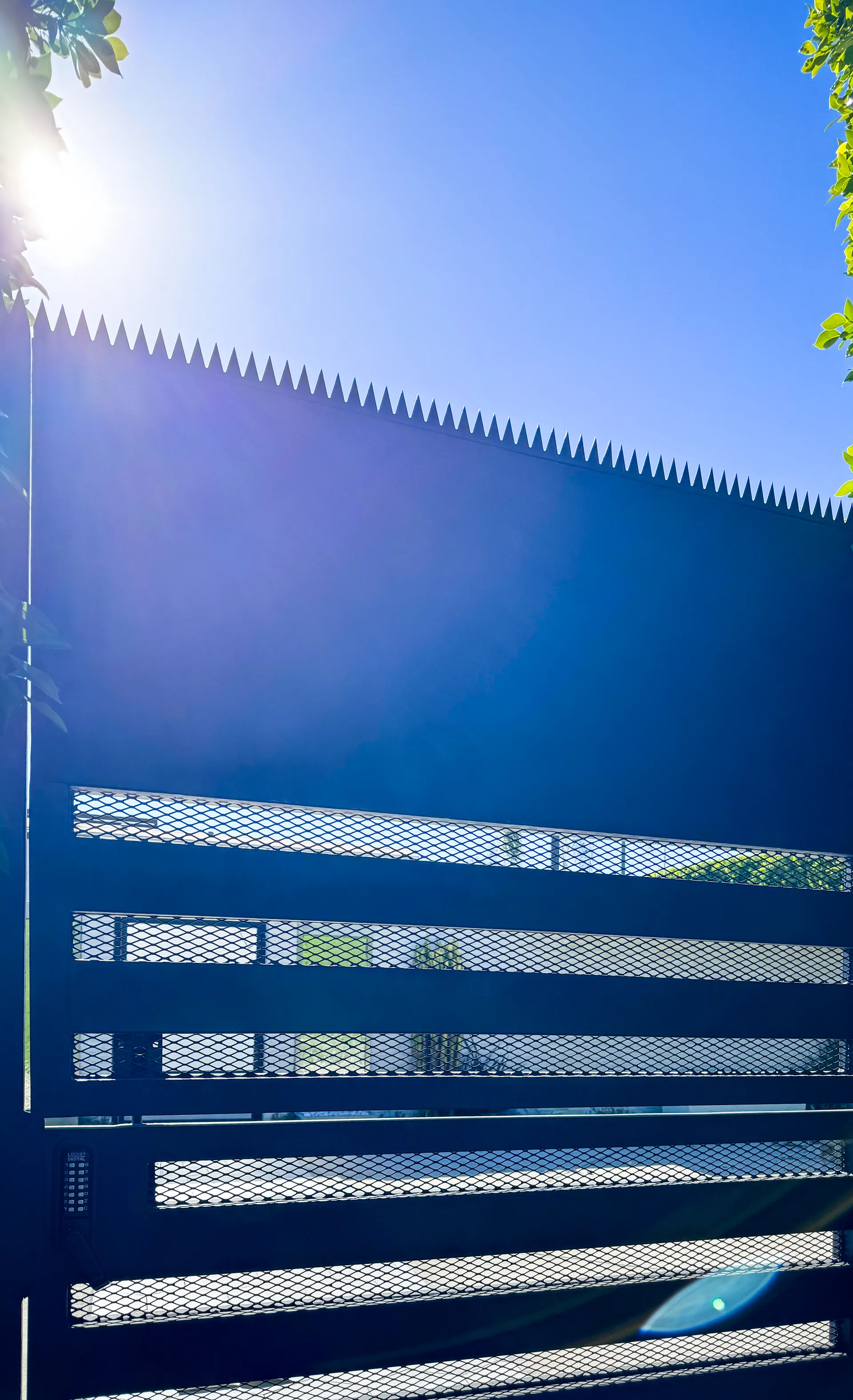 Low-angle shot looking up at anti-climb spikes on top of a black metal gate.