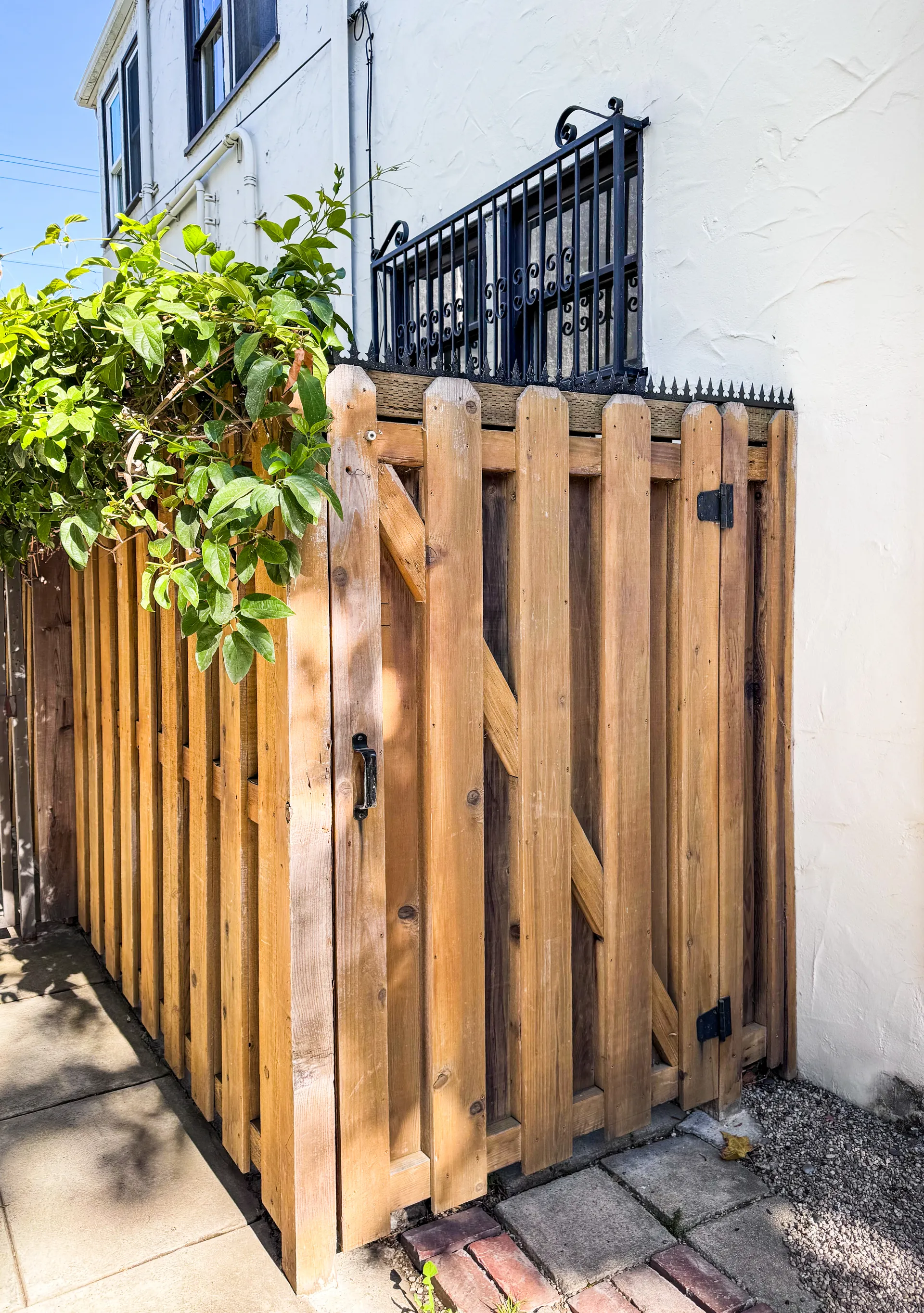 Full view of the narrow side yard entrance. The wooden gate, fence and anti-climb spikes are seen as a unified element.