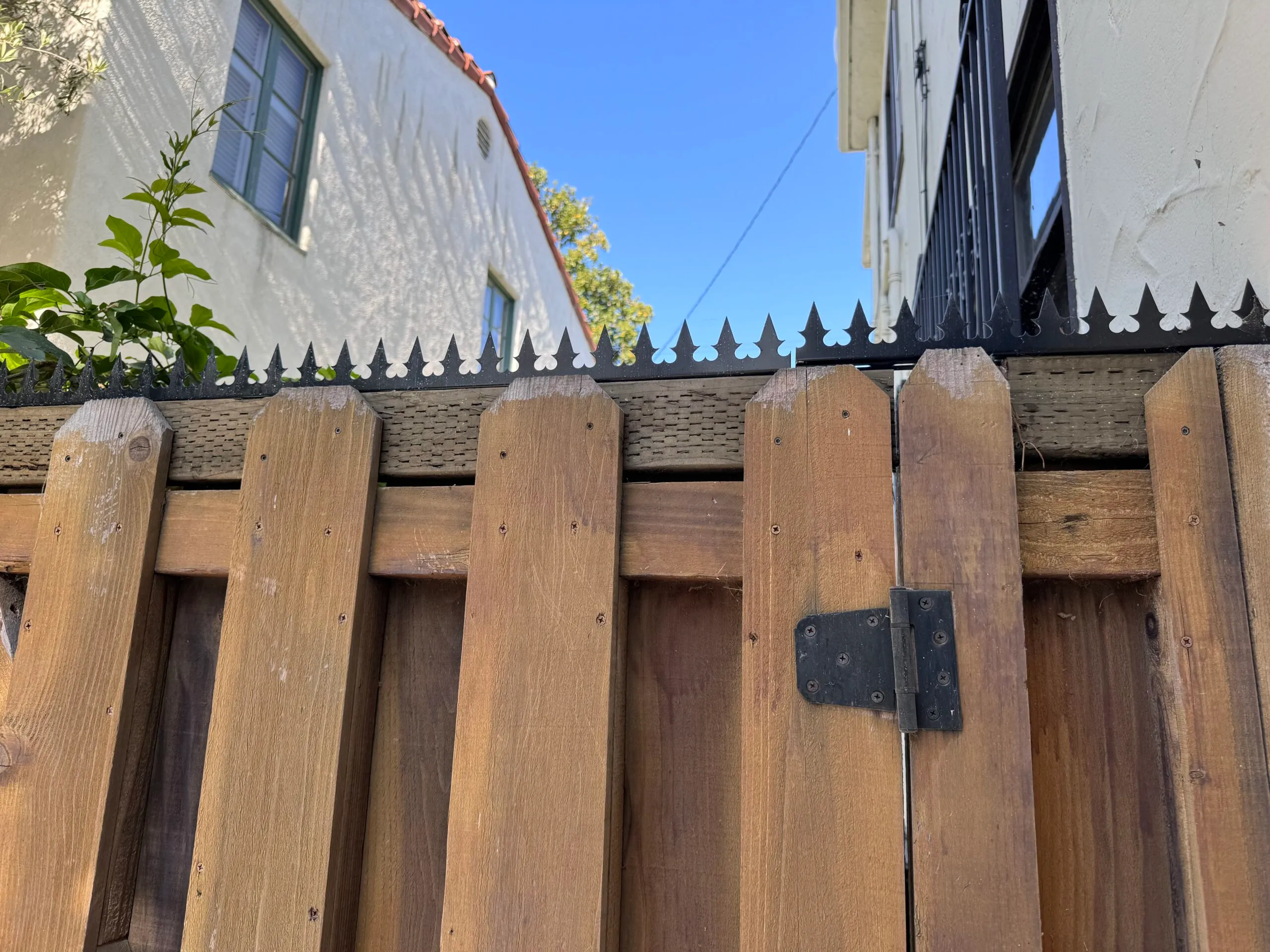 Close-up of the fence top edge. Anti-climb spikes are continuously arranged across the wooden gate and adjacent panels.