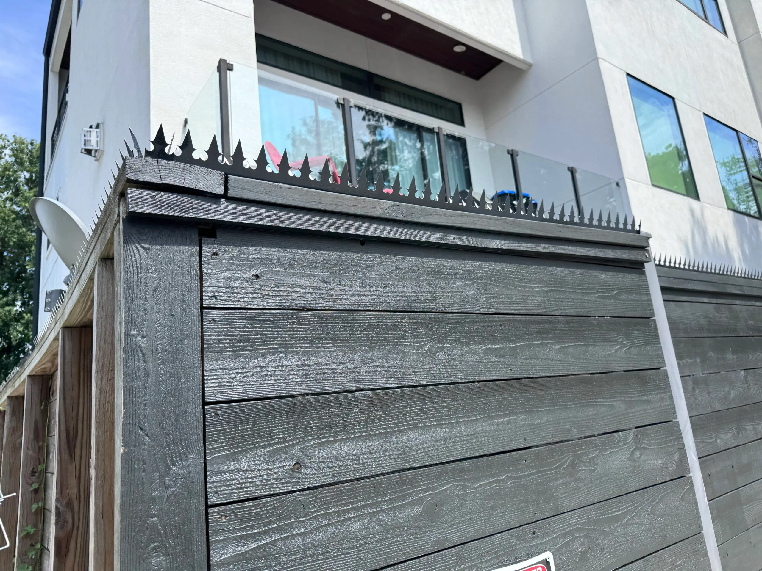 Black Gothic crown on the corner of a charcoal black wooden fence. Next to a modern stucco exterior wall (Stanford St, Houston).