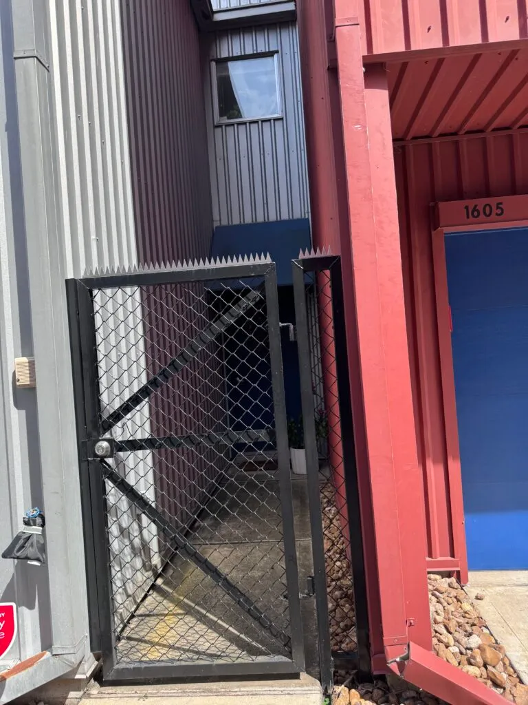 Black framed chain link gate with anti-climb spikes at the top, industrial entry.