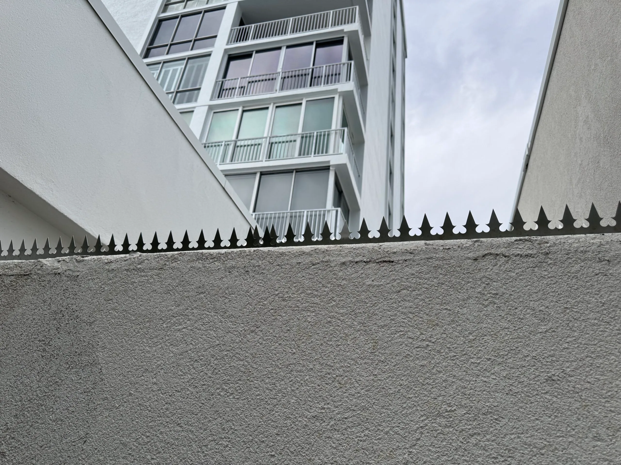 A view from above looking down at security spikes lining a boundary wall, with high-rise towers in the background.