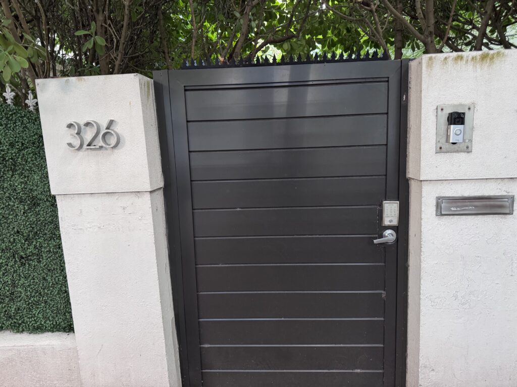 Schwarzes Eingangstor mit weisser Stuckwand in SoFi (Miami Beach). Gothic Anti-Kletter-Spitzen durchgehend auf der Oberkante installiert.
