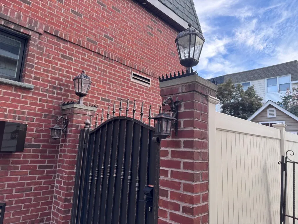 Close-up of brick pillar with lantern and anti-climb spikes on top of black metal gate