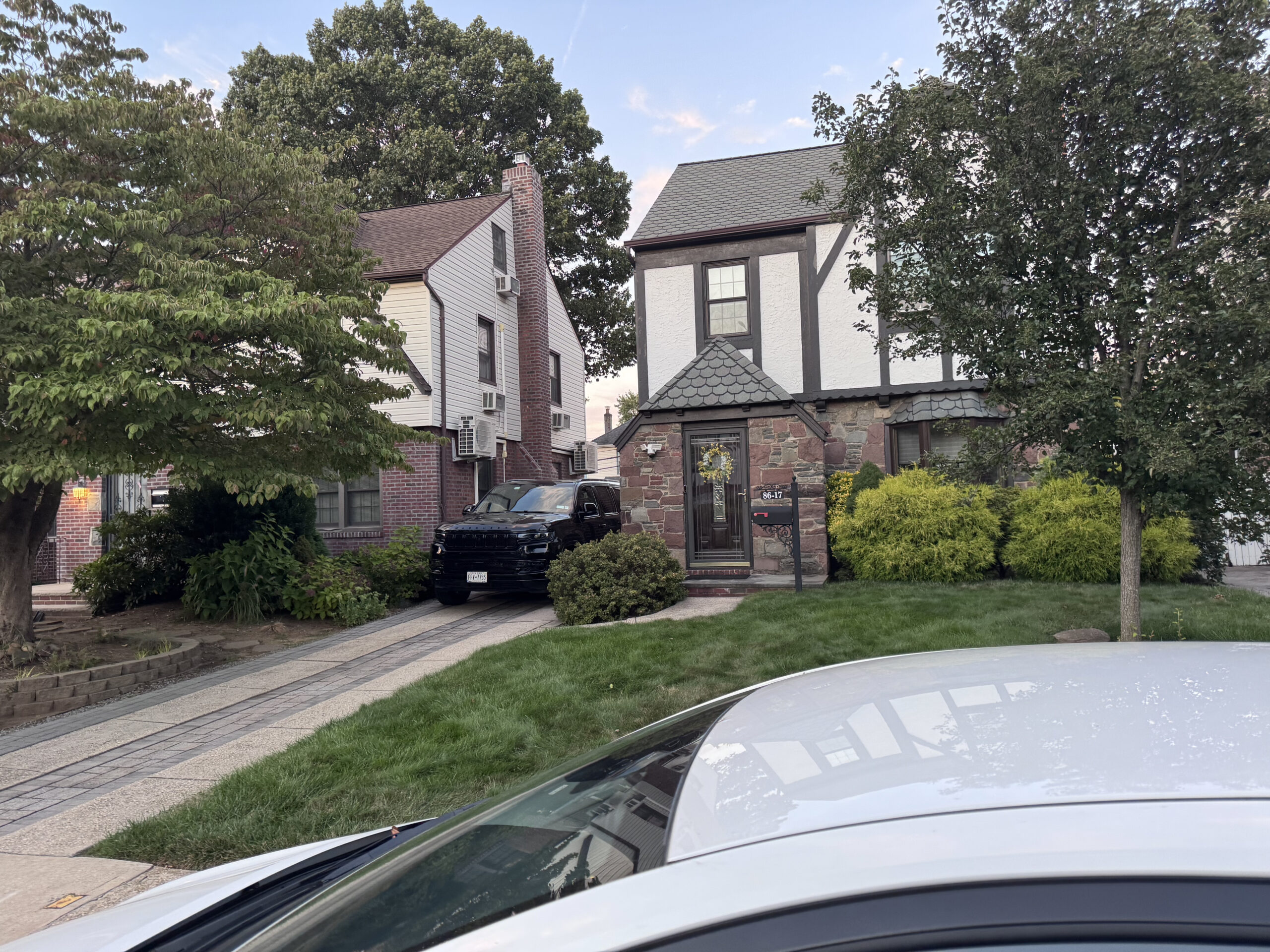 Residencia suburbana de estilo Tudor con paredes de piedra y estuco. Jardín delantero y una SUV negra estacionada en la entrada del garaje.