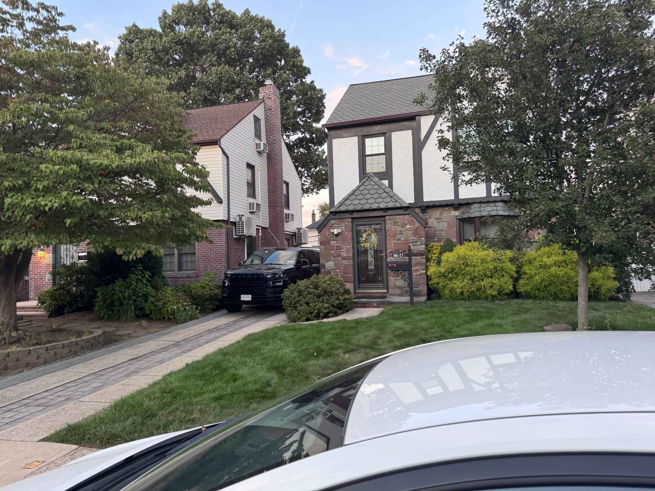 Suburban Tudor-style home with stone and stucco exterior. Front yard and driveway with a black SUV parked.
