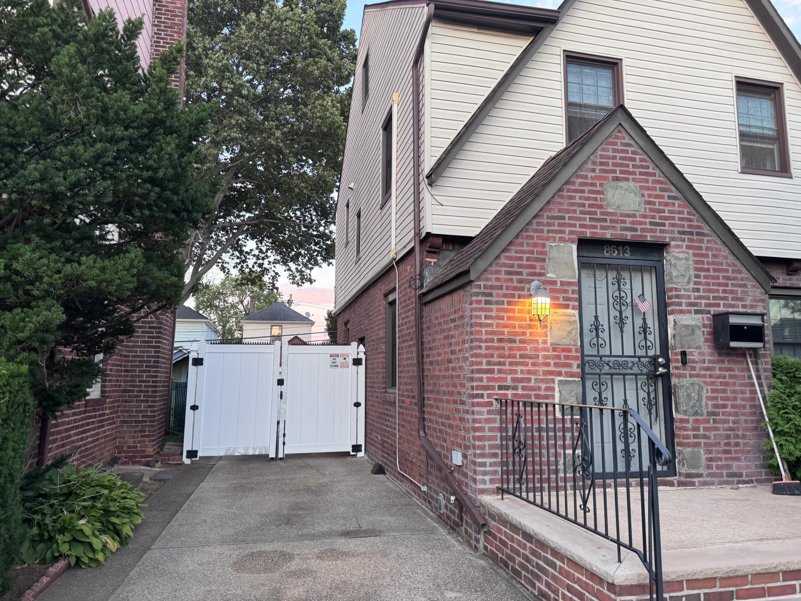 Brick exterior house. Iron front door and stairs, white side gate visible at the end of the driveway.