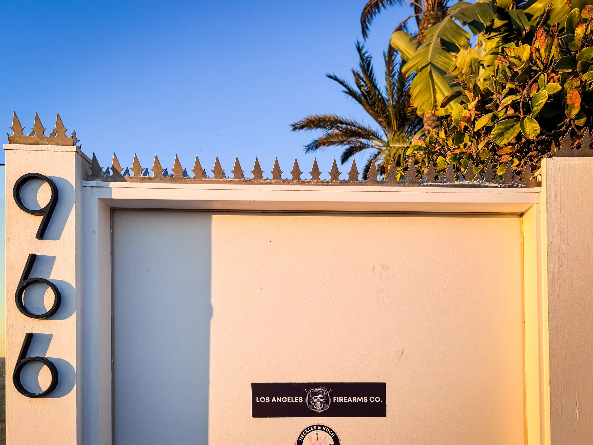 Frosted-glass beachfront privacy wall with anti-climb spikes along the top, ocean and palm-lined horizon beyond, agave plantings in the foreground