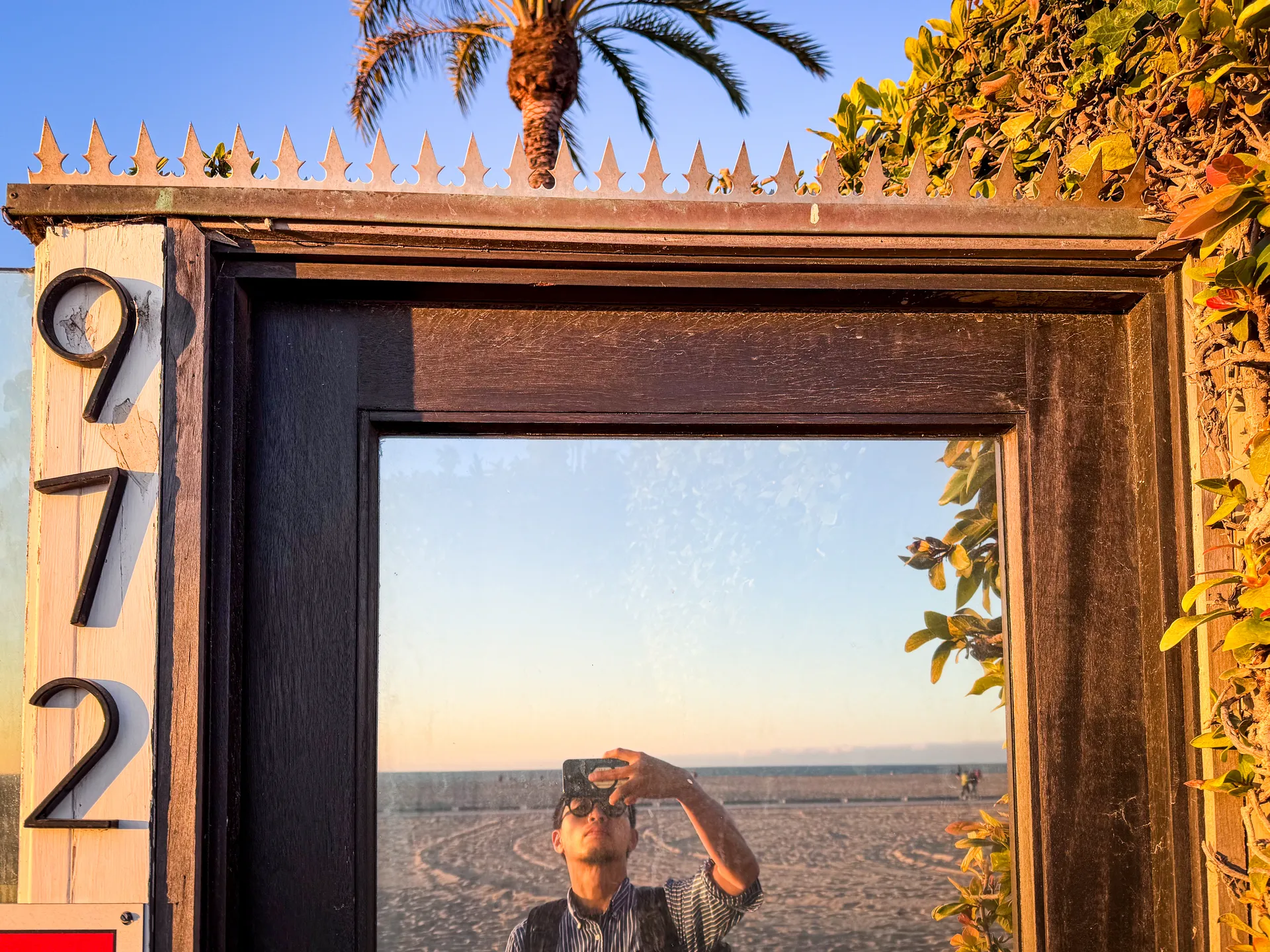 Frosted-glass gate at golden hour with the beach visible through the panel and anti-climb spikes overhead