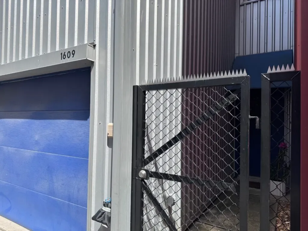 Chain link gate with spikes installed in a narrow passage between buildings.