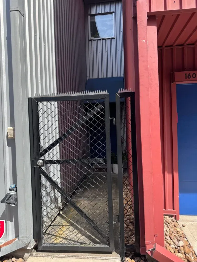 Residential alley between a modern building and a garage. Clear blue sky above.