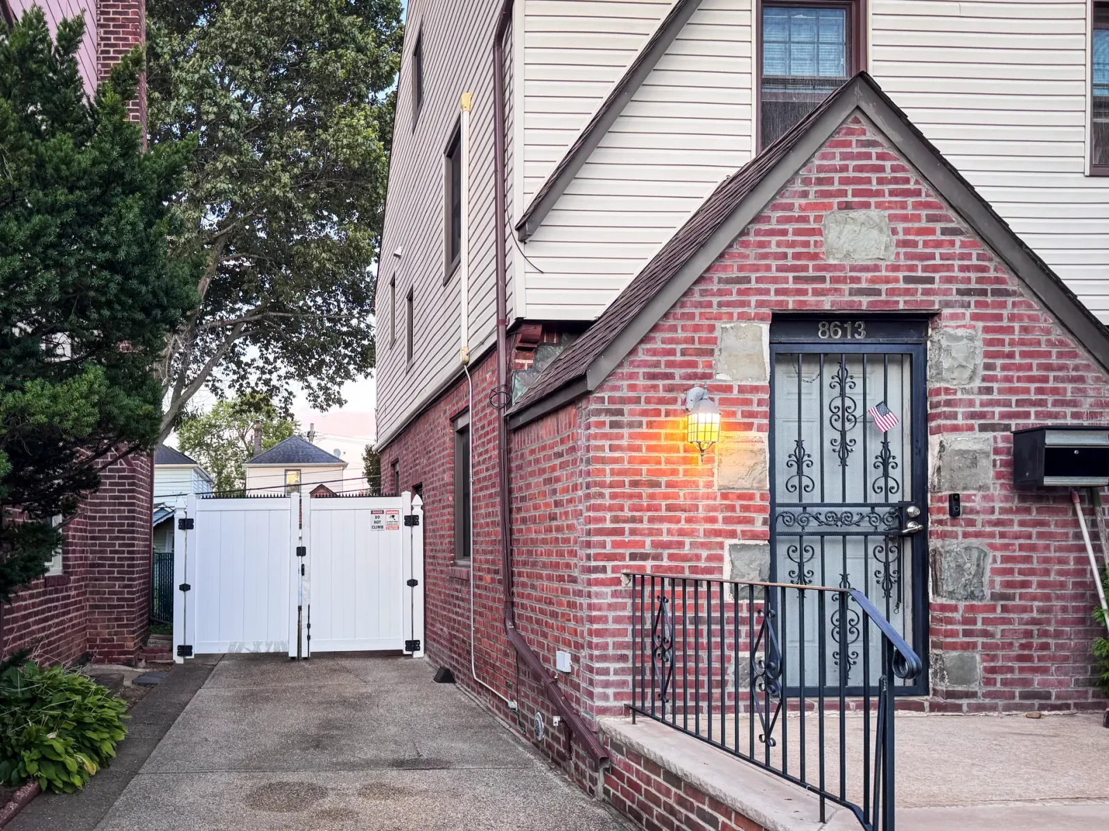 Brick exterior house. Iron front door and stairs, white side gate visible at the end of the driveway.