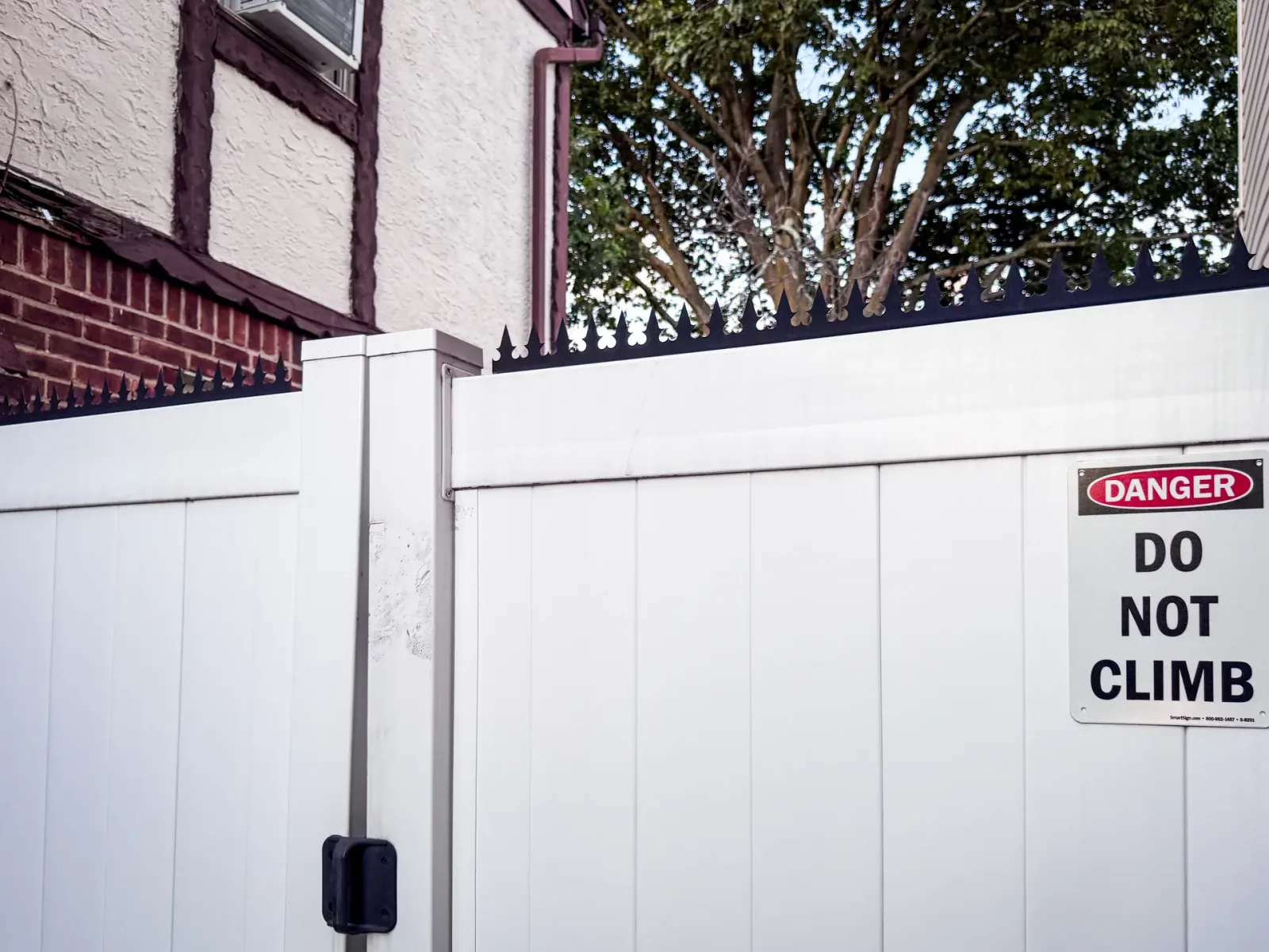 Low-profile black anti-climb spikes installed as a continuous crown on top of a white wood fence.