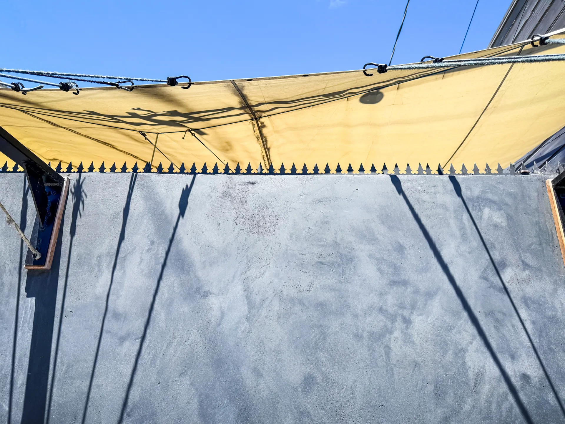 Modern serrated spikes running along the charcoal stucco wall beneath yellow shade sails