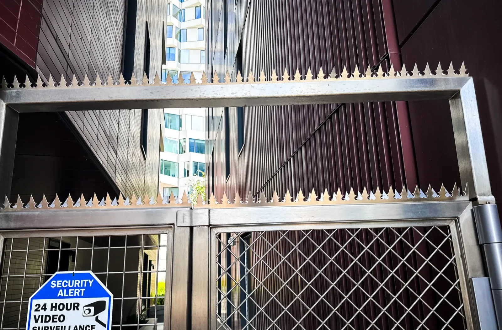 Gros plan d'une clôture métallique à pics de sécurité acérés. Panneau bleu « vidéosurveillance 24 h/24 » visible.