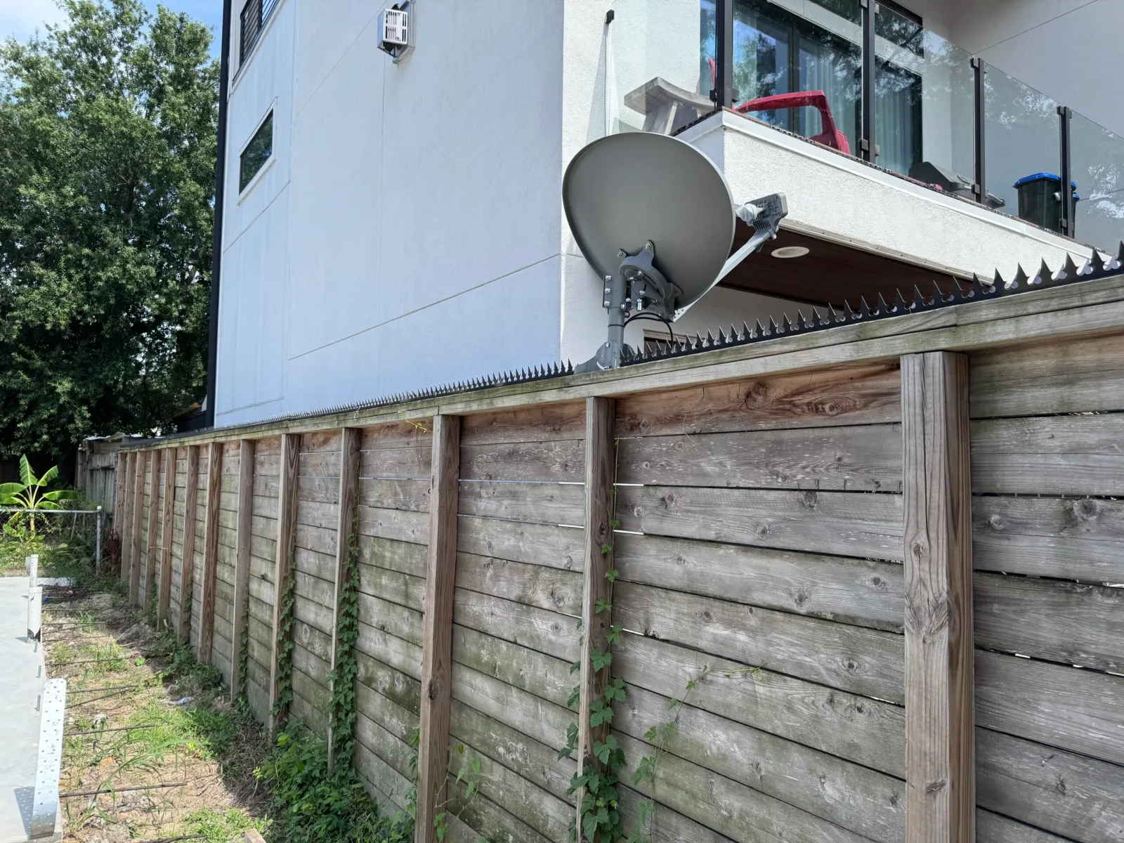 Modernes weißes Haus über einem hohen schwarzen Zaun gesehen. Anti-Kletter-Spikes entlang der Oberkante des Zauns.
