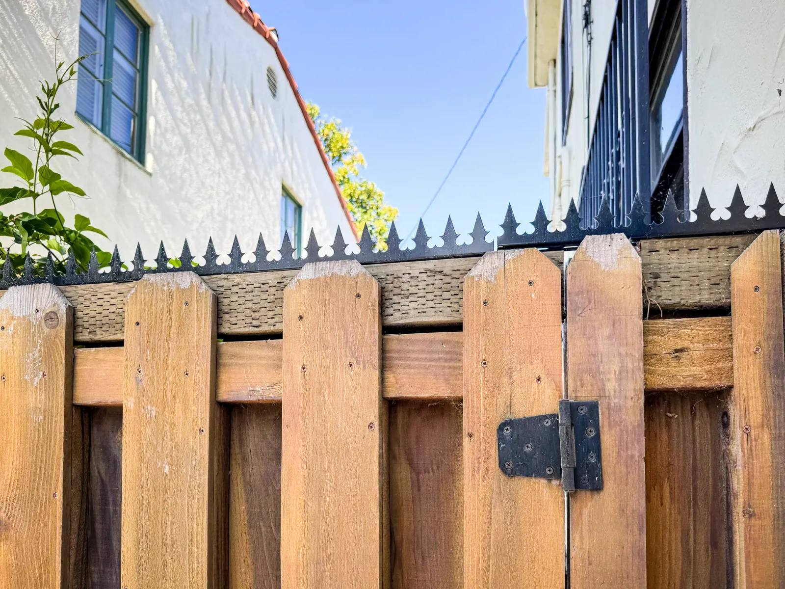 Close-up of the fence top edge. Anti-climb spikes are continuously arranged across the wooden gate and adjacent panels.