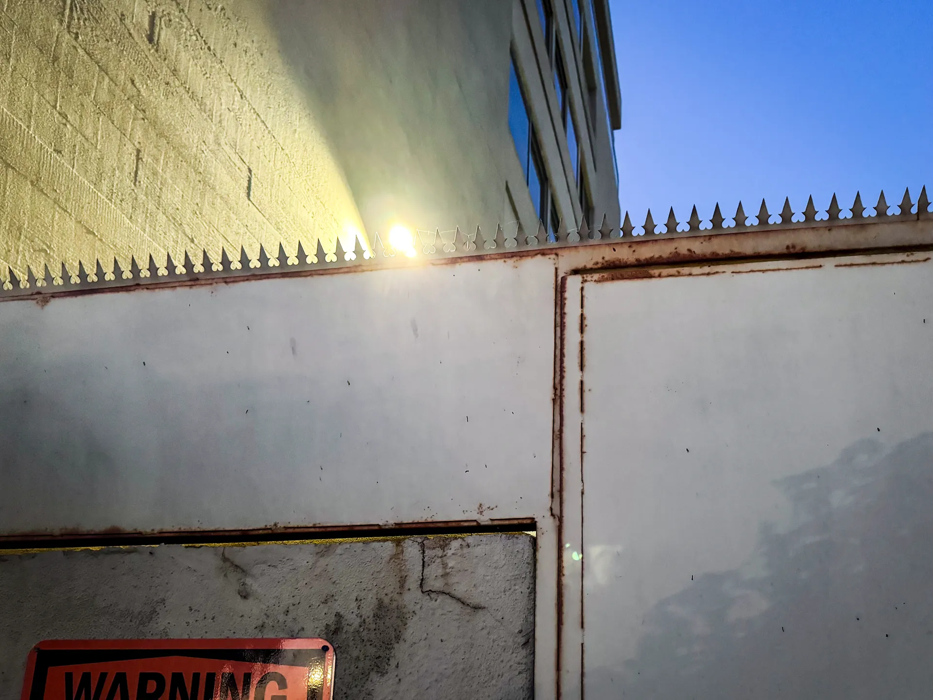 Spiked top edge of the white perimeter wall meeting an adjacent building