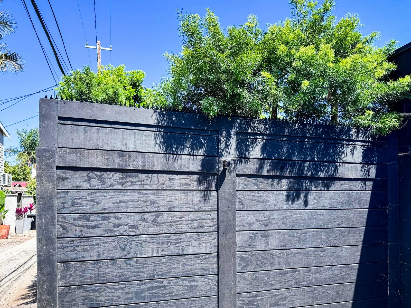 Black wood driveway gate with anti-climb spikes along the top edge under a clear blue sky.
