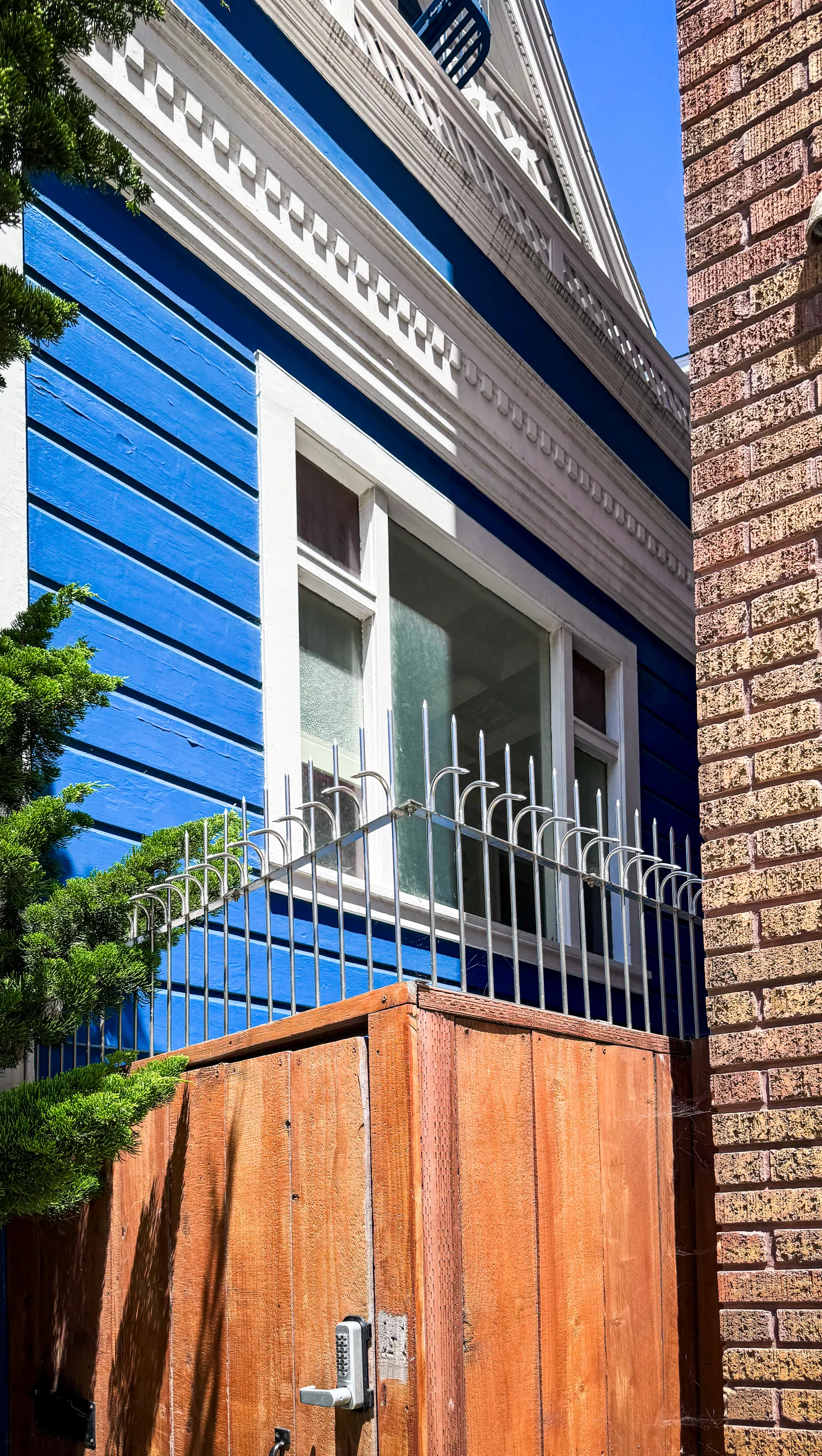 Stainless hook-type anti-climb spikes mounted on the metal fence above a wooden side gate