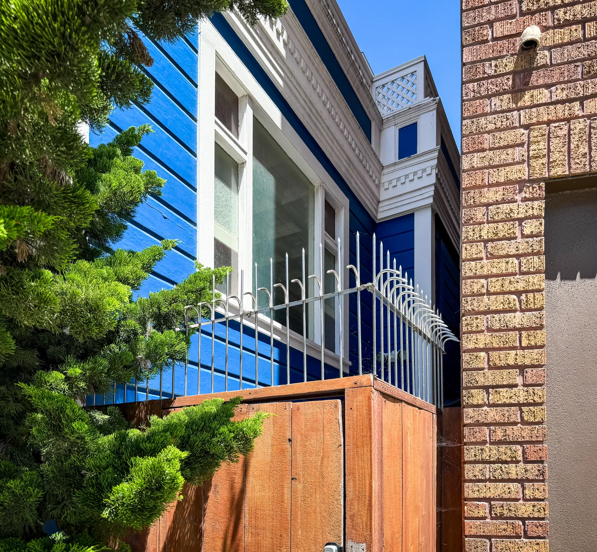Side passage between the blue Victorian home and the brick building, protected by anti-climb spikes