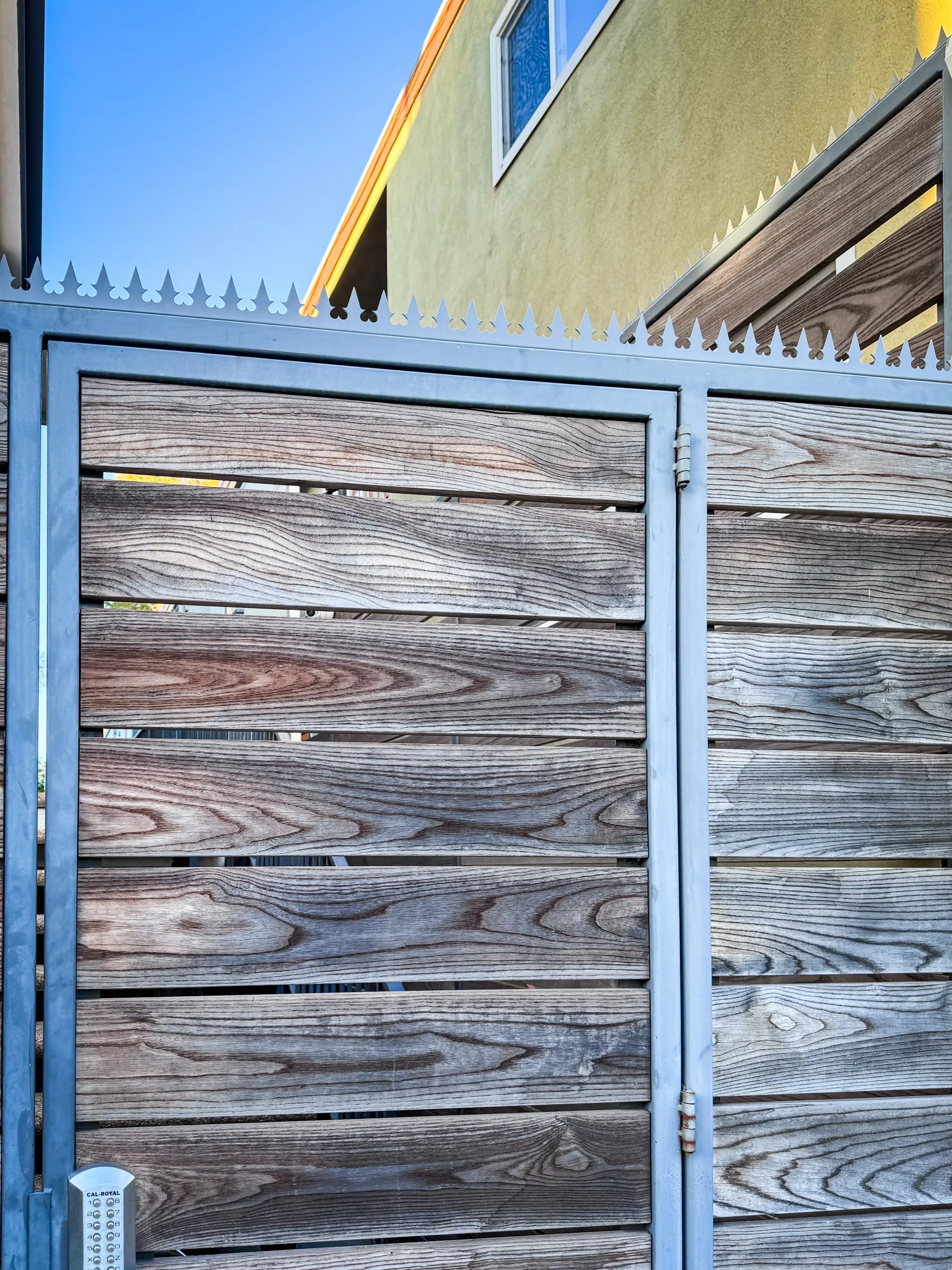 Close-up of the gray slatted pedestrian gate with anti-climb spikes along the top rail