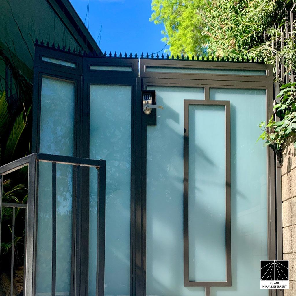 GIZAGIZA black heart-shaped security spikes installed on top of a modern frosted glass gate – Japanese-made deterrent uniting privacy, design, and protection