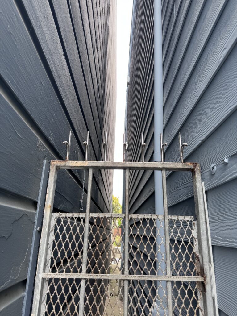 Metal security gate with anti-climb spikes in a narrow alley between two buildings