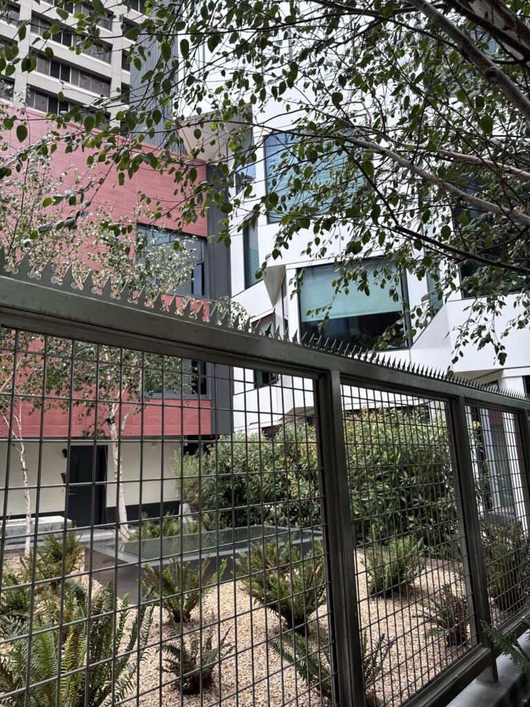 Anti-climb security spikes installed on a metal mesh fence in a landscaped courtyard