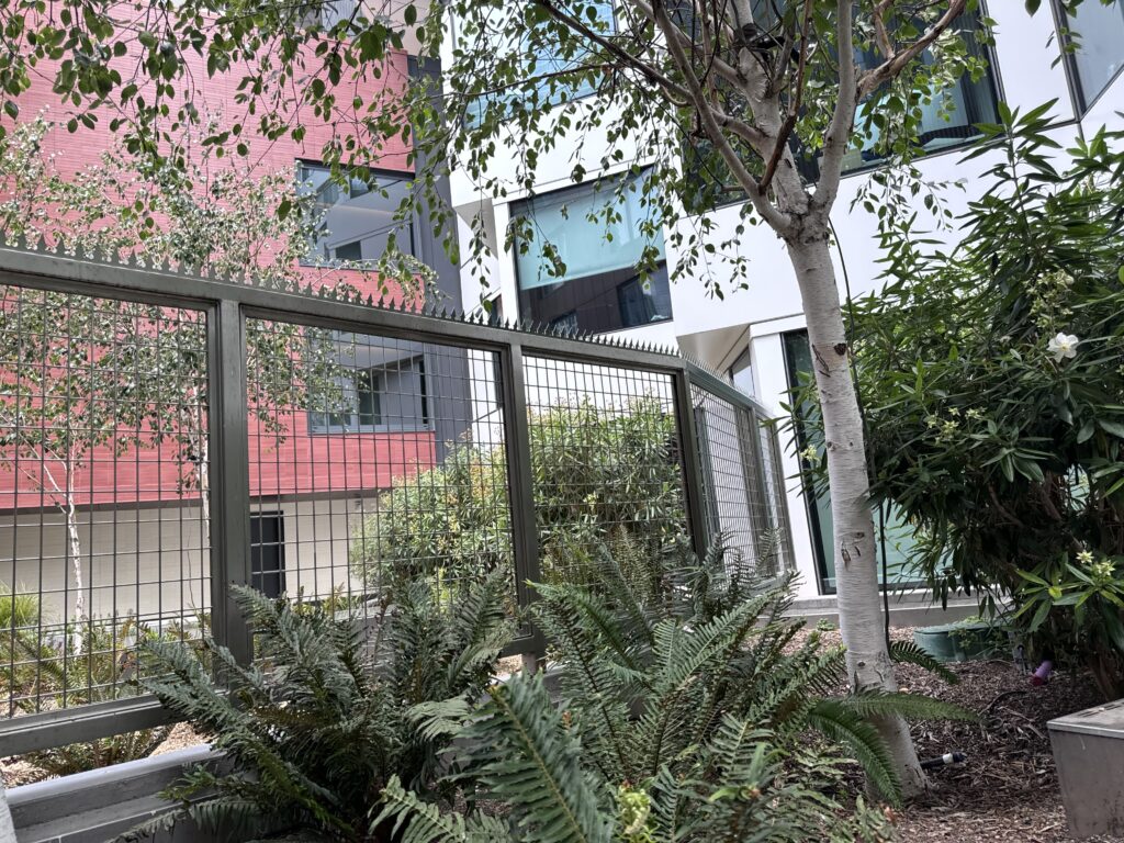 Metal security fence with anti-climb spikes, courtyard plants, and apartment building exterior