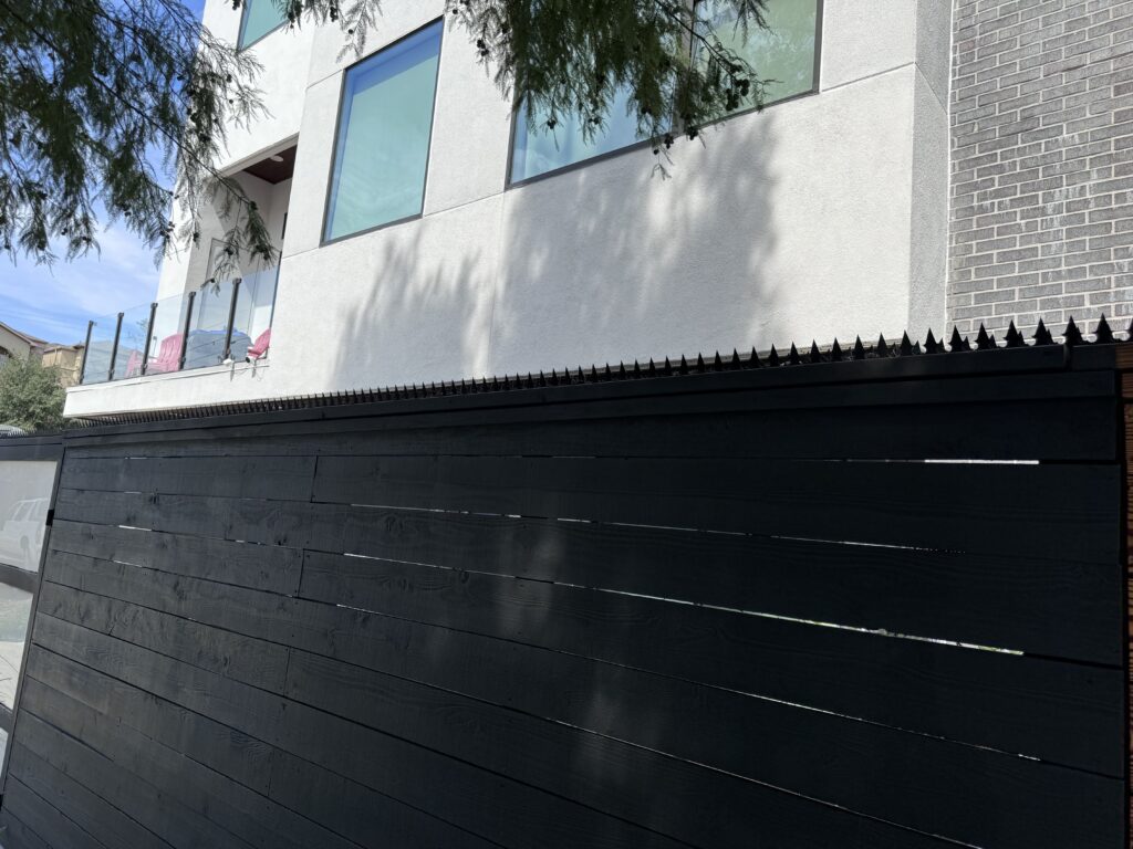 Corner view of a black wooden fence with anti-climb spikes below a glass-railed balcony