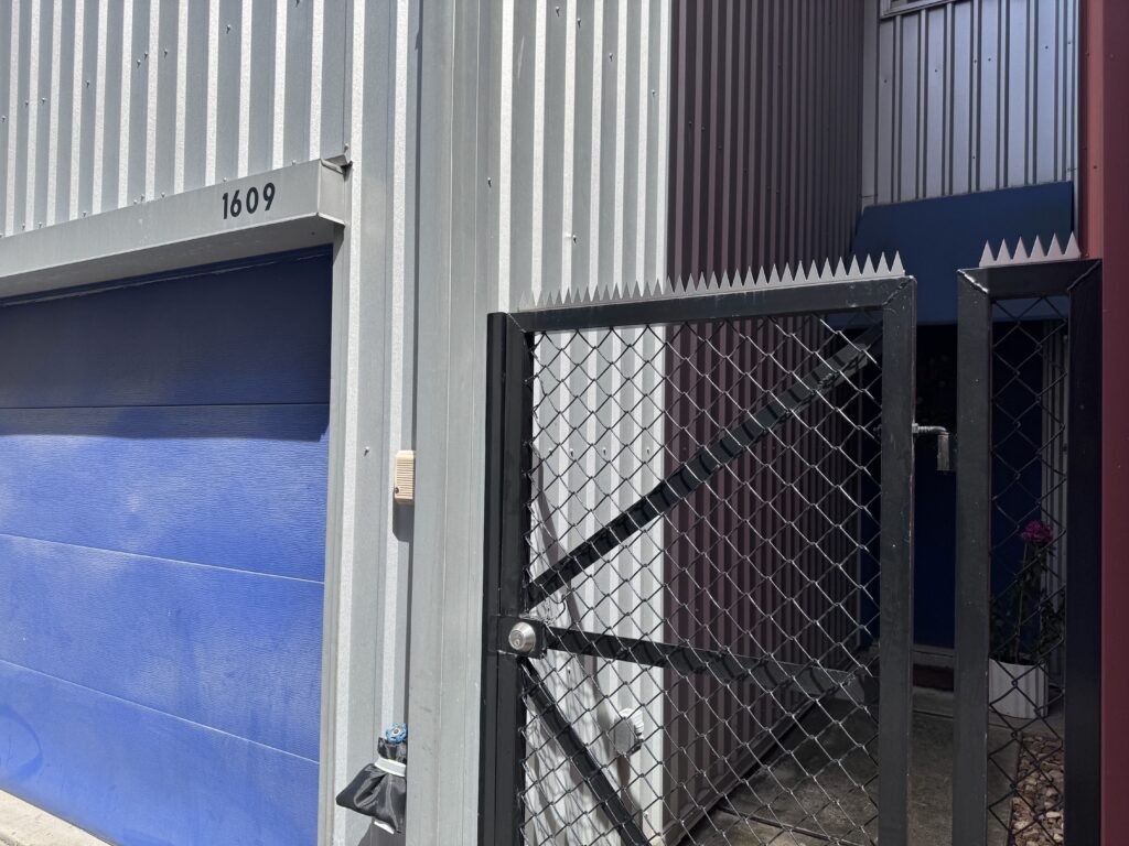 Chain-link gate with security spikes installed, narrow passage between buildings