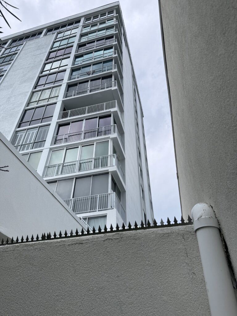 Vue d'angle d'un mur en stuc surmonté de pointes de sécurité entre deux bâtiments.