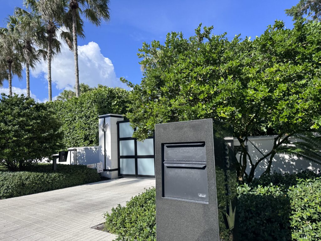 Mailbox in the foreground with a frosted glass gate and landscaped entrance behind