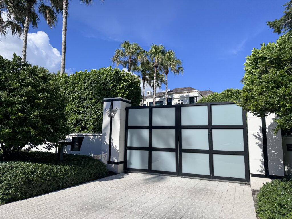 Front view of a frosted glass driveway gate with white pillars and greenery