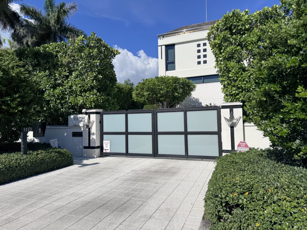 Modern home entrance with a frosted glass driveway gate and lush greenery
