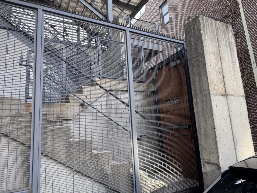 Cerca de metal com pontas de segurança em frente a uma escada externa de aço industrial.