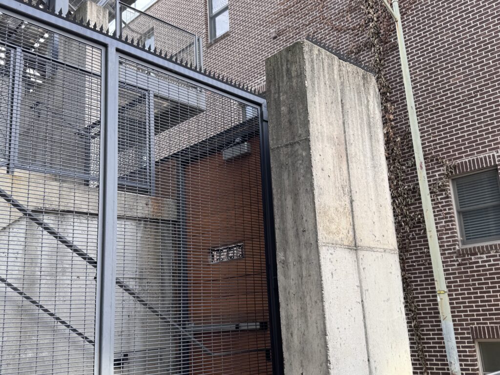 Columna de hormigón armado y valla metálica con protección superior contra intrusos.