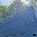 Ninja Deterrent Sicherheitsspitzen auf einem Holztor mit Überwachungskamera – kombinierter mechanischer und elektronischer Einbruchschutz.