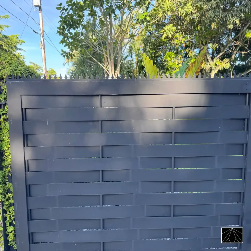 Barrera de seguridad Ninja Deterrent Gothic en color blanco sobre un portón de lamas negro en un entorno tropical, ofreciendo protección perimetral con un alto contraste estético.