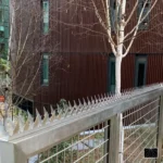 Espigões de segurança Ninja Deterrent transparentes instalados em cerca de malha metálica comercial para proteção invisível.