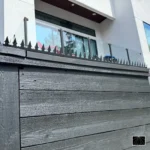 Piques anti-escalade Ninja Deterrent Gothic noirs sur une clôture en bois avec garde-corps en verre, une solution de sécurité pour design contemporain.