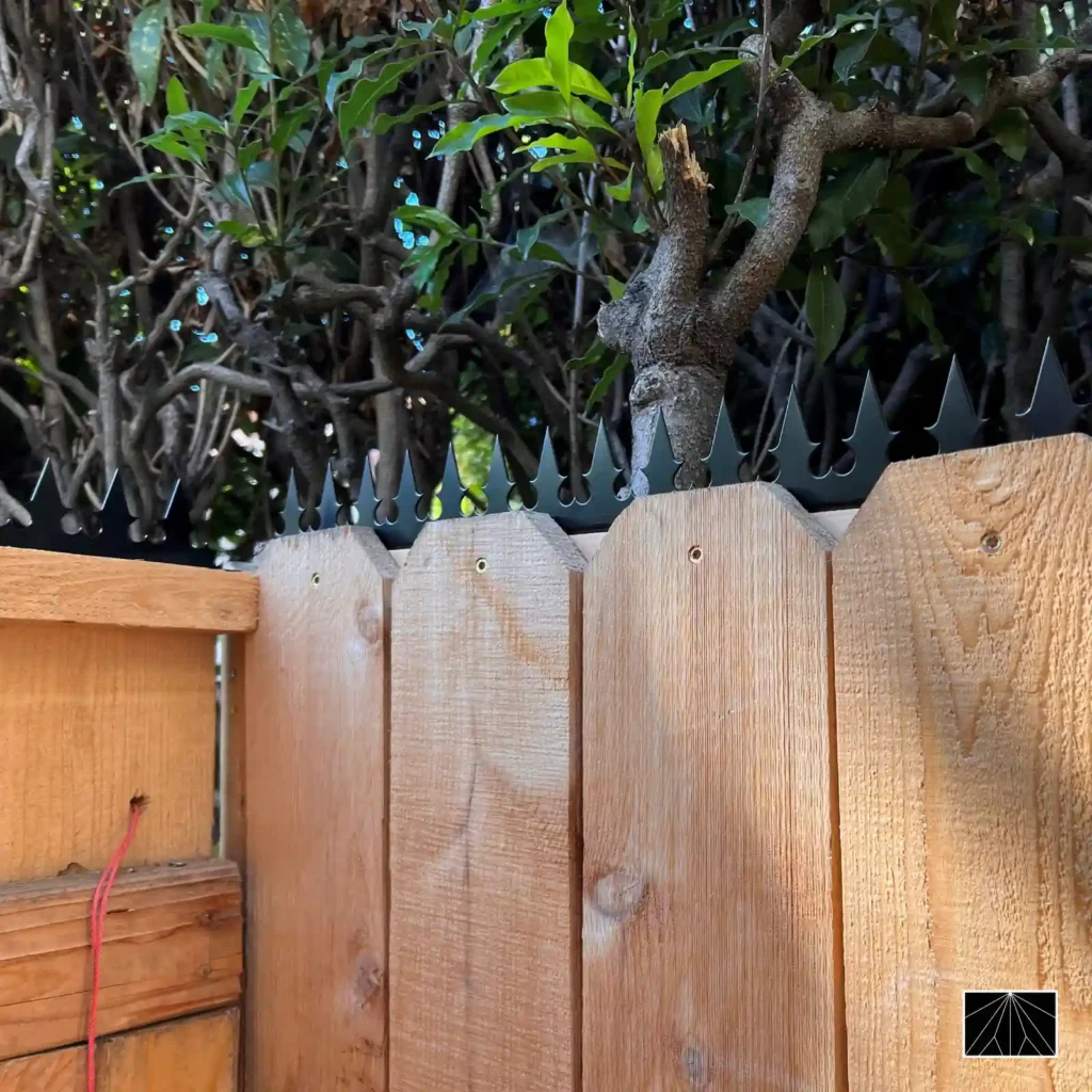 Gros plan des pointes de sécurité Ninja Deterrent Gothic en noir sur une clôture en bois, créant un contraste protecteur et rustique.