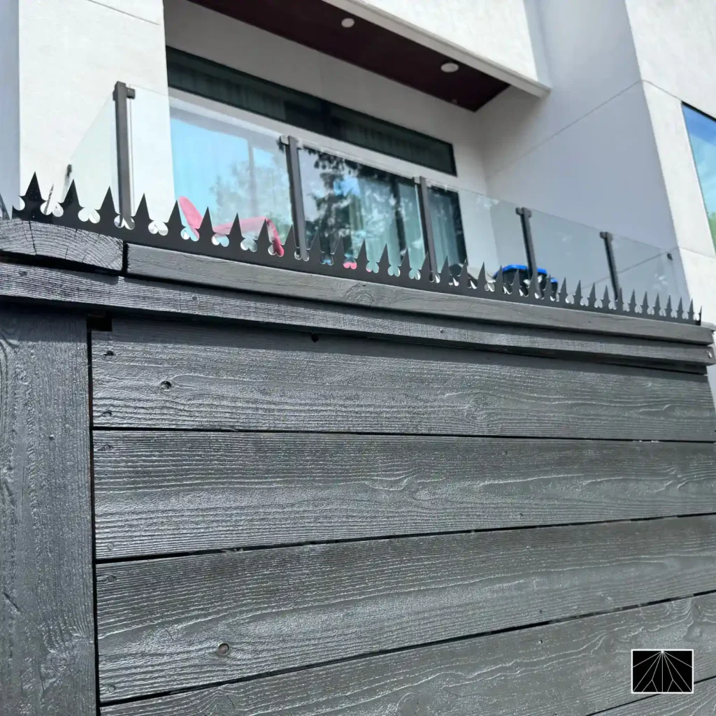 Espetos anti-escalada Ninja Deterrent Gothic pretos em cerca de madeira com guarda-corpo de vidro, solução de segurança moderna.
