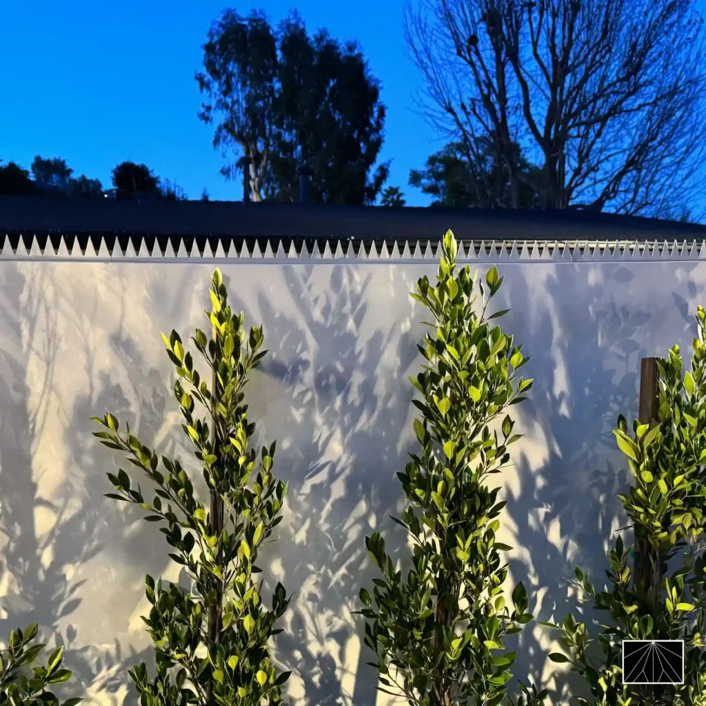 安装于住宅围墙的 Ninja Deterrent 现代系列白色防攀尖刺，极简主义设计与植物光影。